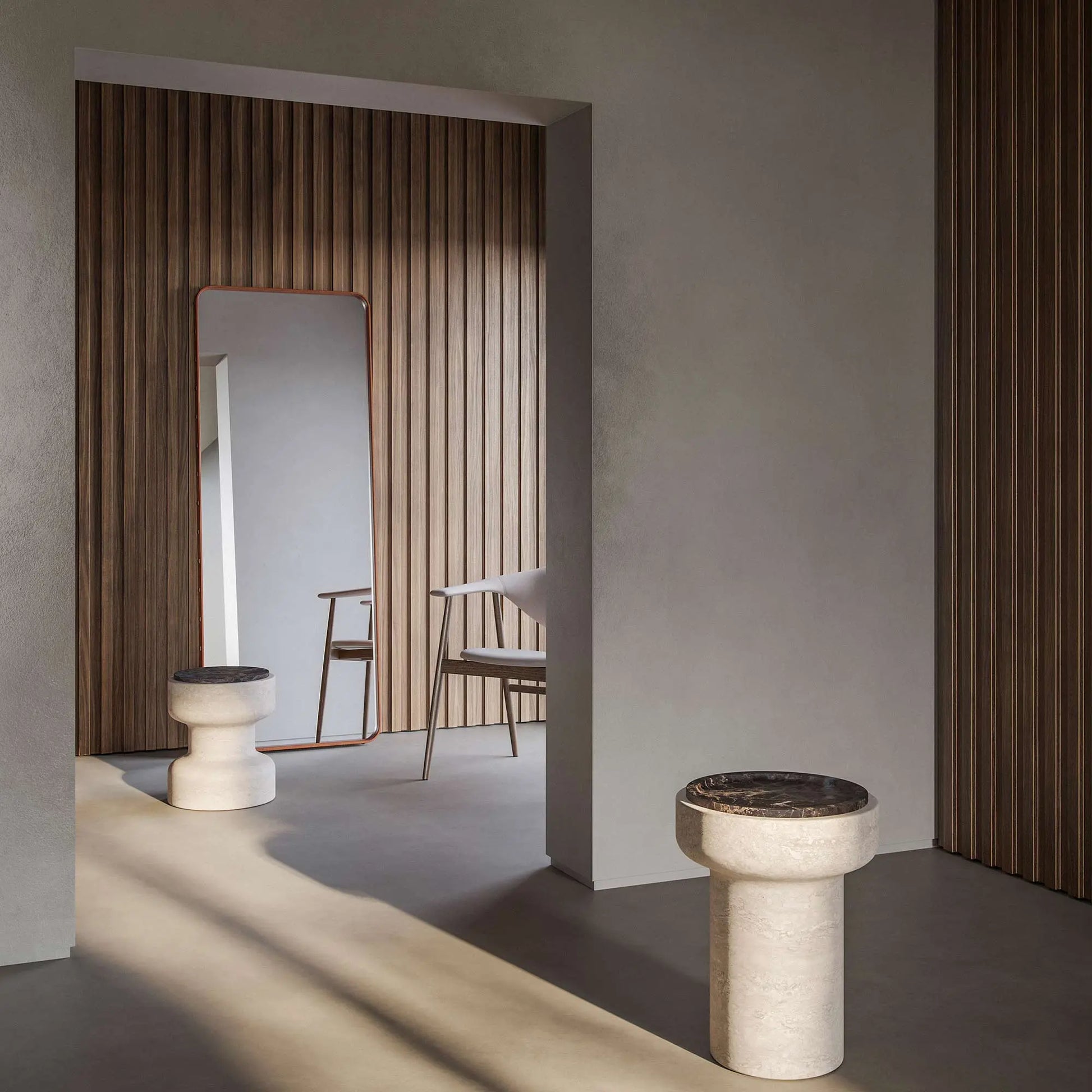 Tivoli stool in Travertino Navona base and Black Emperador (bottom left). In a room with a mirror and a chair with wood paneled wall in background. In the foreground, a Tivoli table with Black Emperador top.