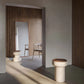 Tivoli stool in Travertino Navona base and Walnut wood top (bottom left). In a room with a mirror and a chair with wood paneled wall in background. In the foreground, a Tivoli table with Walnut wood top.