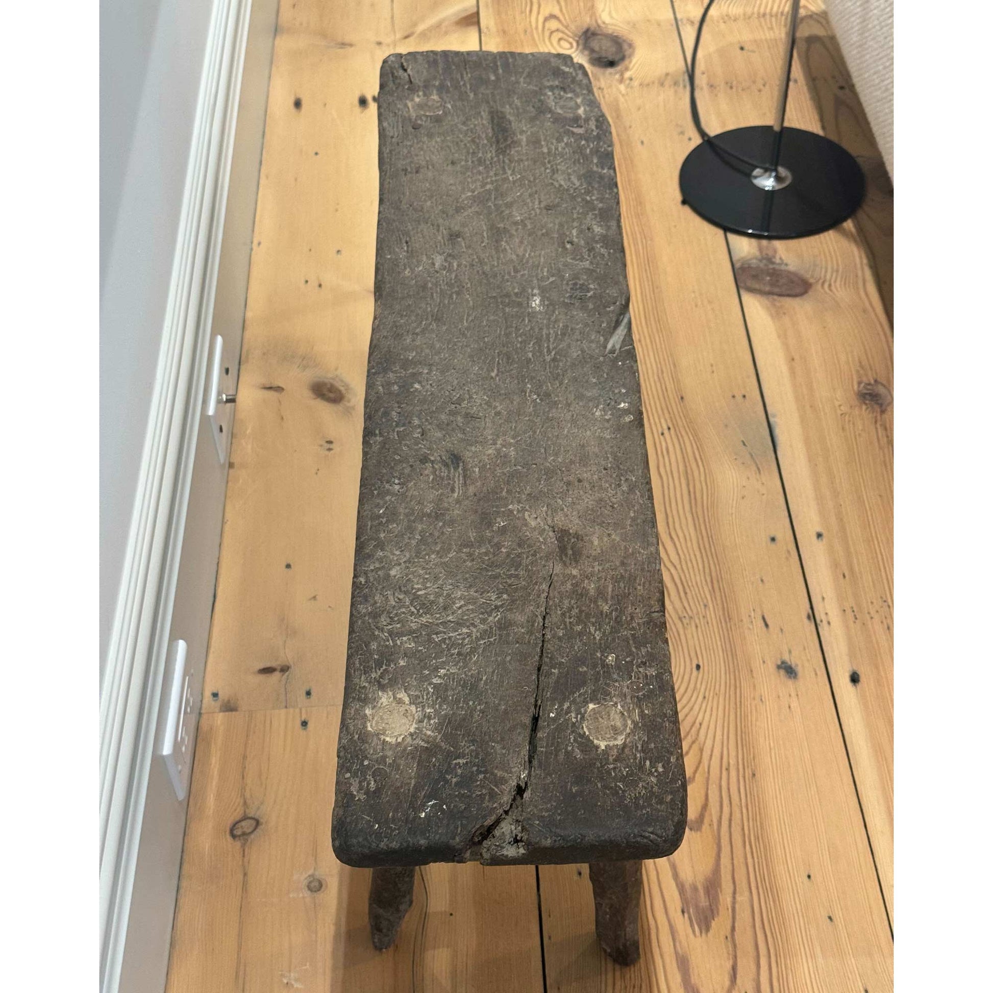 Top view of Antique small table made of dark brown wood in a room with white background and hardwood floors. Partial view of the bottom of a black standing lamp can be seen in the top right of image. 